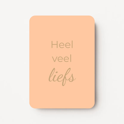 Staand minikaartje met goudbeige tekst ‘Heel veel liefs’, minimalistisch ontwerp op een zachte abrikooskleurige achtergrond, flatlay op witte ondergrond.
