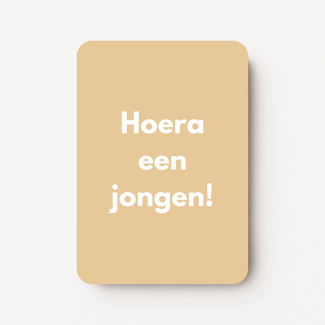 Staand minikaartje met tekst ‘Hoera een jongen!’ in witte letters, minimalistisch ontwerp op zachte honingbeige achtergrond, flatlay op witte ondergrond.