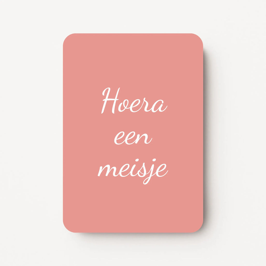 Staand minikaartje met tekst ‘Hoera een meisje’ in witte letters, minimalistisch ontwerp op warme oudroze achtergrond, flatlay op witte ondergrond.