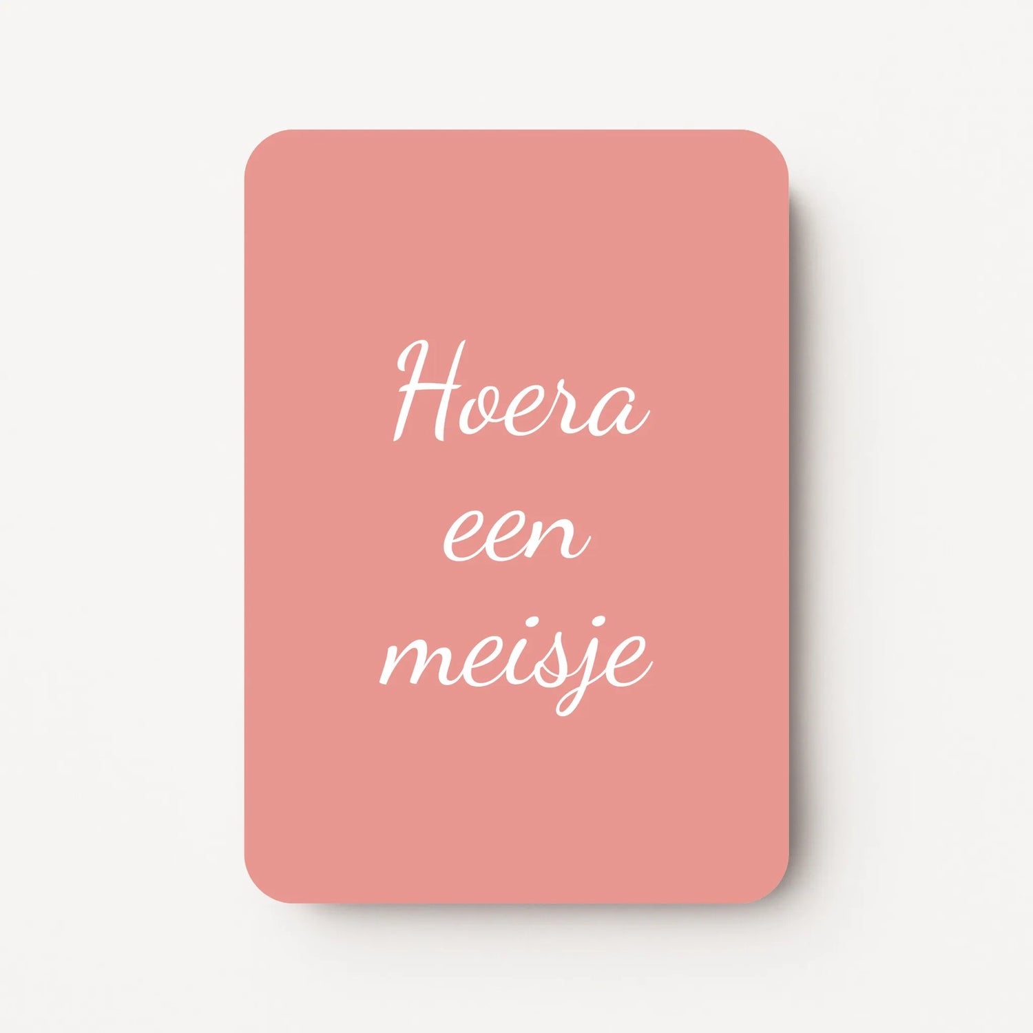 Staand minikaartje met tekst ‘Hoera een meisje’ in witte letters, minimalistisch ontwerp op warme oudroze achtergrond, flatlay op witte ondergrond.