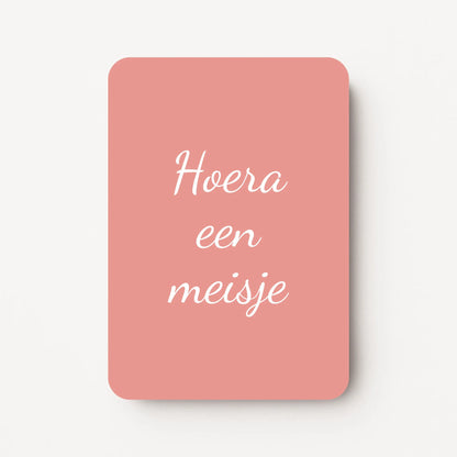 Staand minikaartje met tekst ‘Hoera een meisje’ in witte letters, minimalistisch ontwerp op warme oudroze achtergrond, flatlay op witte ondergrond.