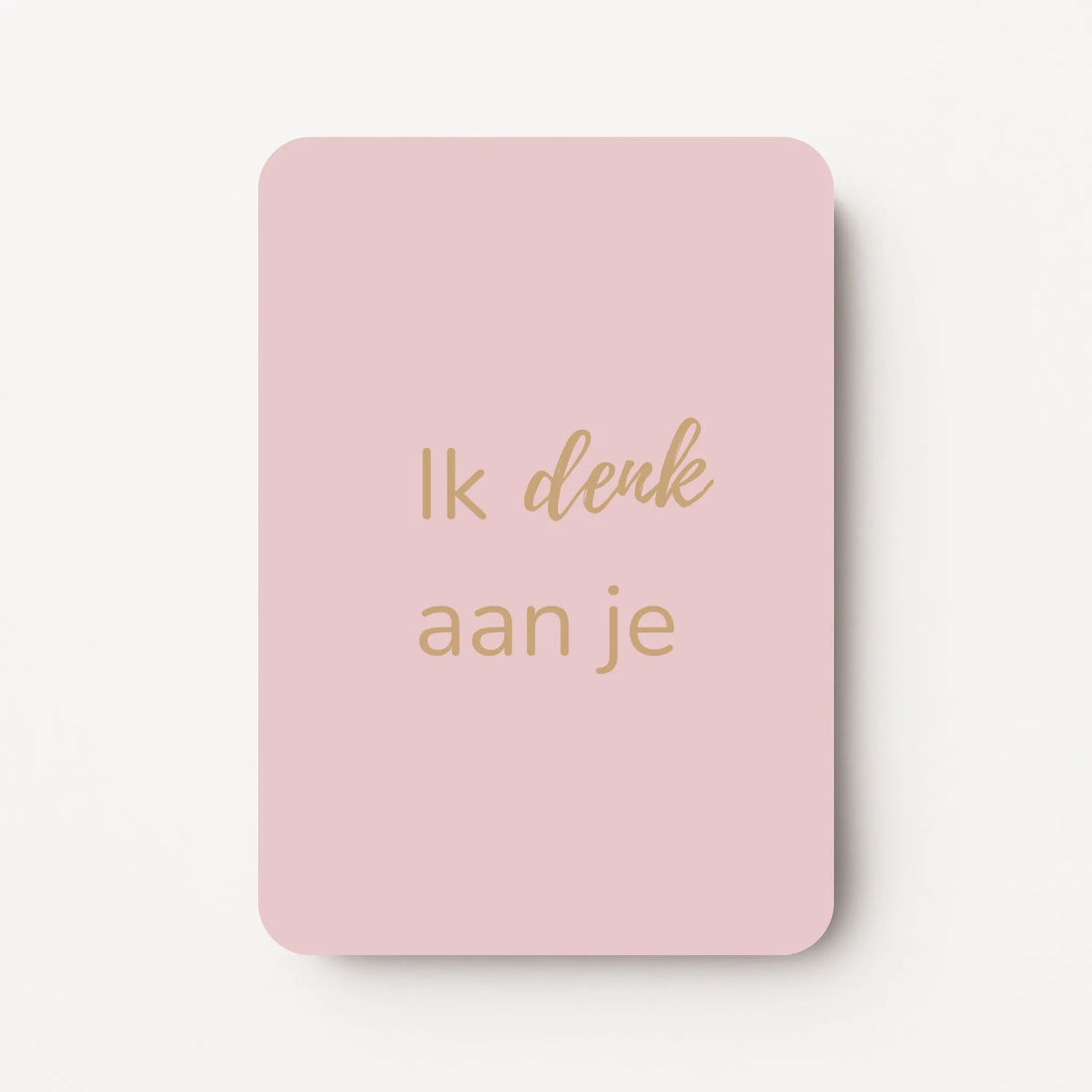 Staand minikaartje met goudbeige tekst ‘Ik denk aan je’, minimalistisch ontwerp op een zachte lichtroze achtergrond, flatlay op witte ondergrond.