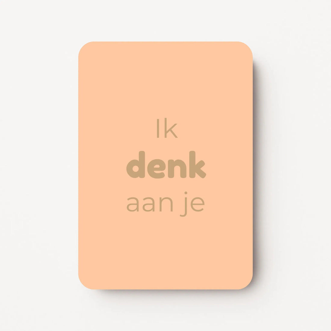 Staand minikaartje met tekst ‘Ik denk aan je’ in goudbeige letters, minimalistisch ontwerp op een warme perzikroze achtergrond, flatlay op witte ondergrond.