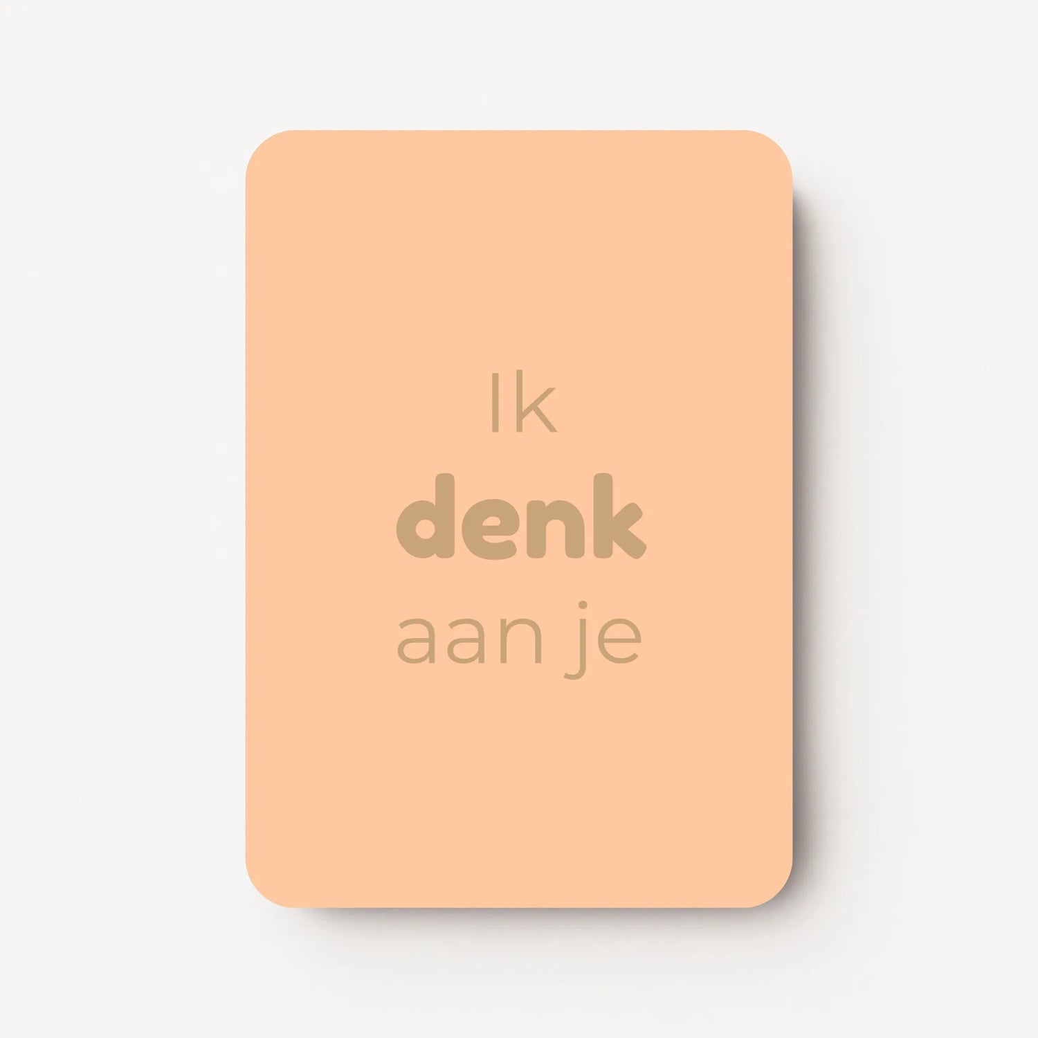 Staand minikaartje met tekst ‘Ik denk aan je’ in goudbeige letters, minimalistisch ontwerp op een warme perzikroze achtergrond, flatlay op witte ondergrond.