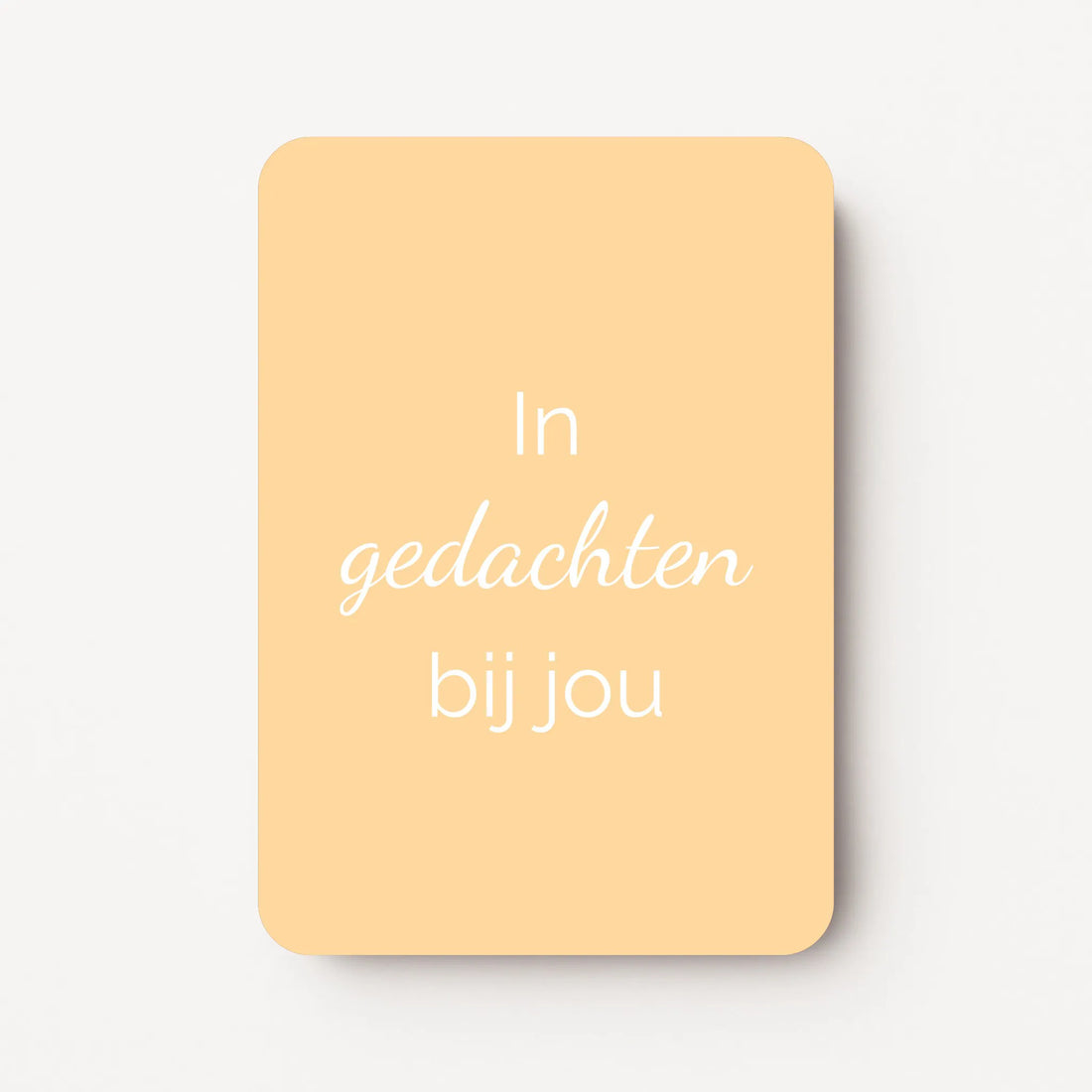 Staand minikaartje met witte tekst ‘In gedachten bij jou’, minimalistisch ontwerp op een warme lichtgele achtergrond, flatlay op witte ondergrond.