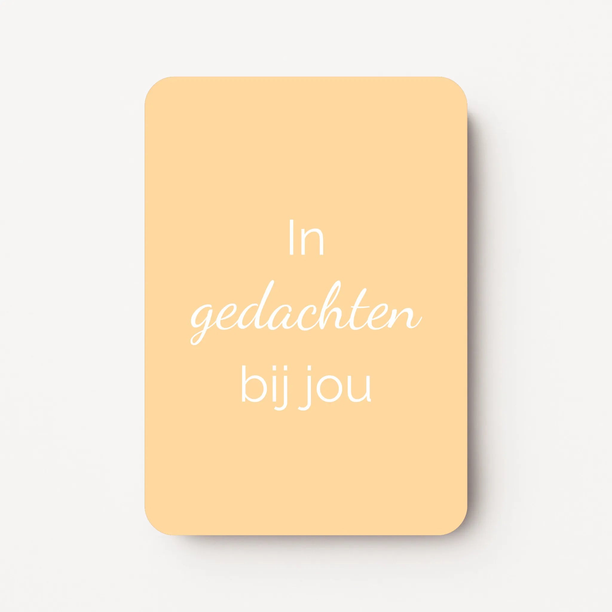 Staand minikaartje met witte tekst ‘In gedachten bij jou’, minimalistisch ontwerp op een warme lichtgele achtergrond, flatlay op witte ondergrond.