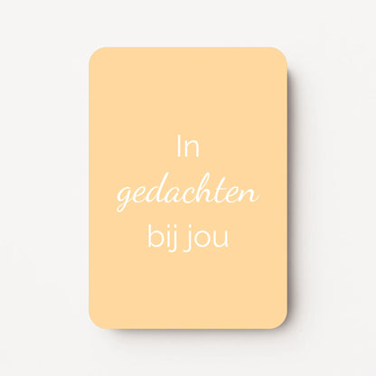 Staand minikaartje met witte tekst ‘In gedachten bij jou’, minimalistisch ontwerp op een warme lichtgele achtergrond, flatlay op witte ondergrond.