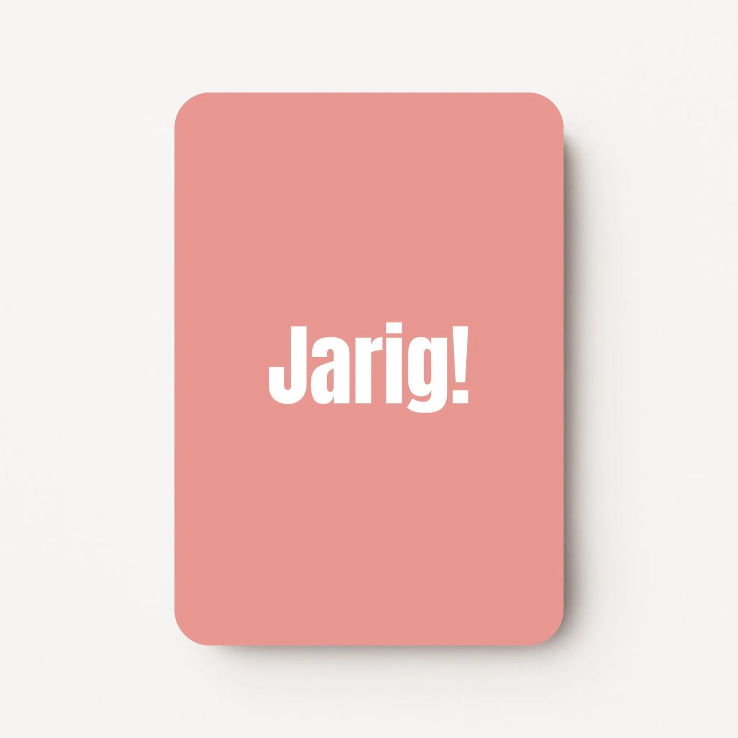 Staand minikaartje met witte tekst ‘Jarig!’, minimalistisch ontwerp op zachte roodroze achtergrond, flatlay op witte ondergrond.