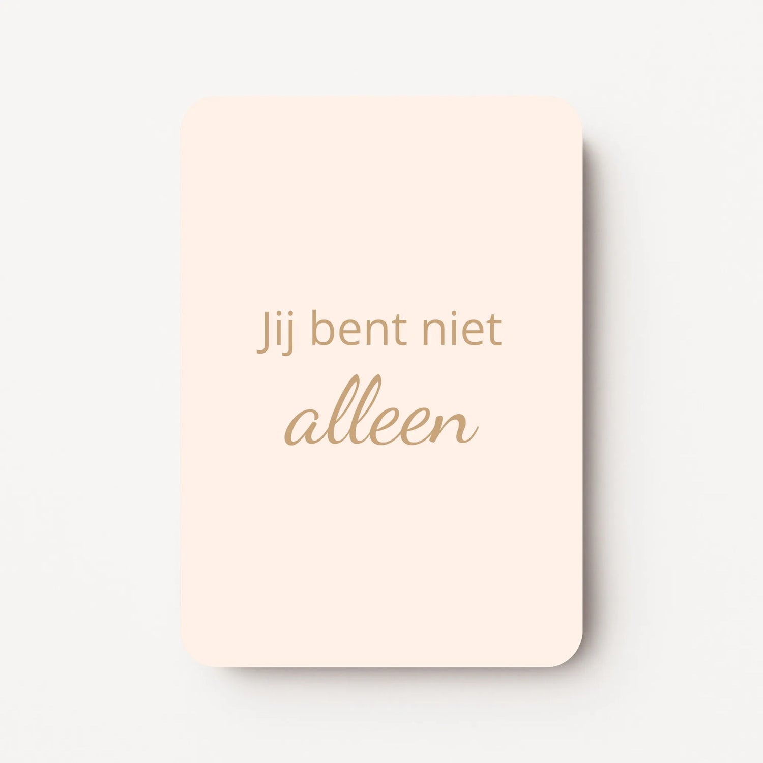 Staand minikaartje met goudbeige tekst ‘Jij bent niet alleen’, minimalistisch ontwerp op een warme perzik-zachtroze achtergrond, flatlay op witte ondergrond.