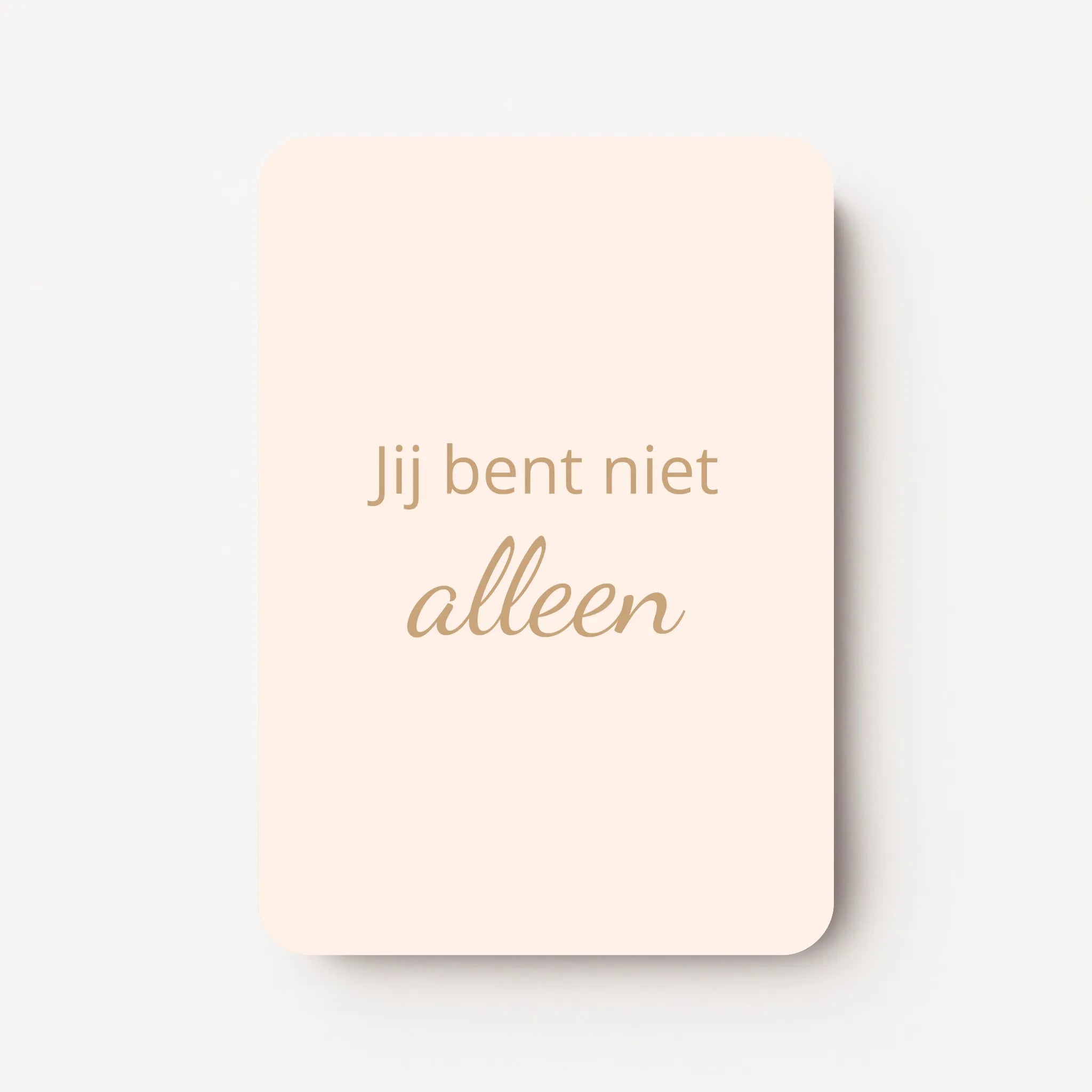 Staand minikaartje met goudbeige tekst ‘Jij bent niet alleen’, minimalistisch ontwerp op een warme perzik-zachtroze achtergrond, flatlay op witte ondergrond.