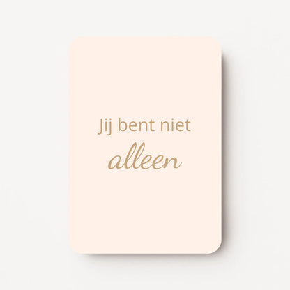 Staand minikaartje met goudbeige tekst ‘Jij bent niet alleen’, minimalistisch ontwerp op een warme perzik-zachtroze achtergrond, flatlay op witte ondergrond.