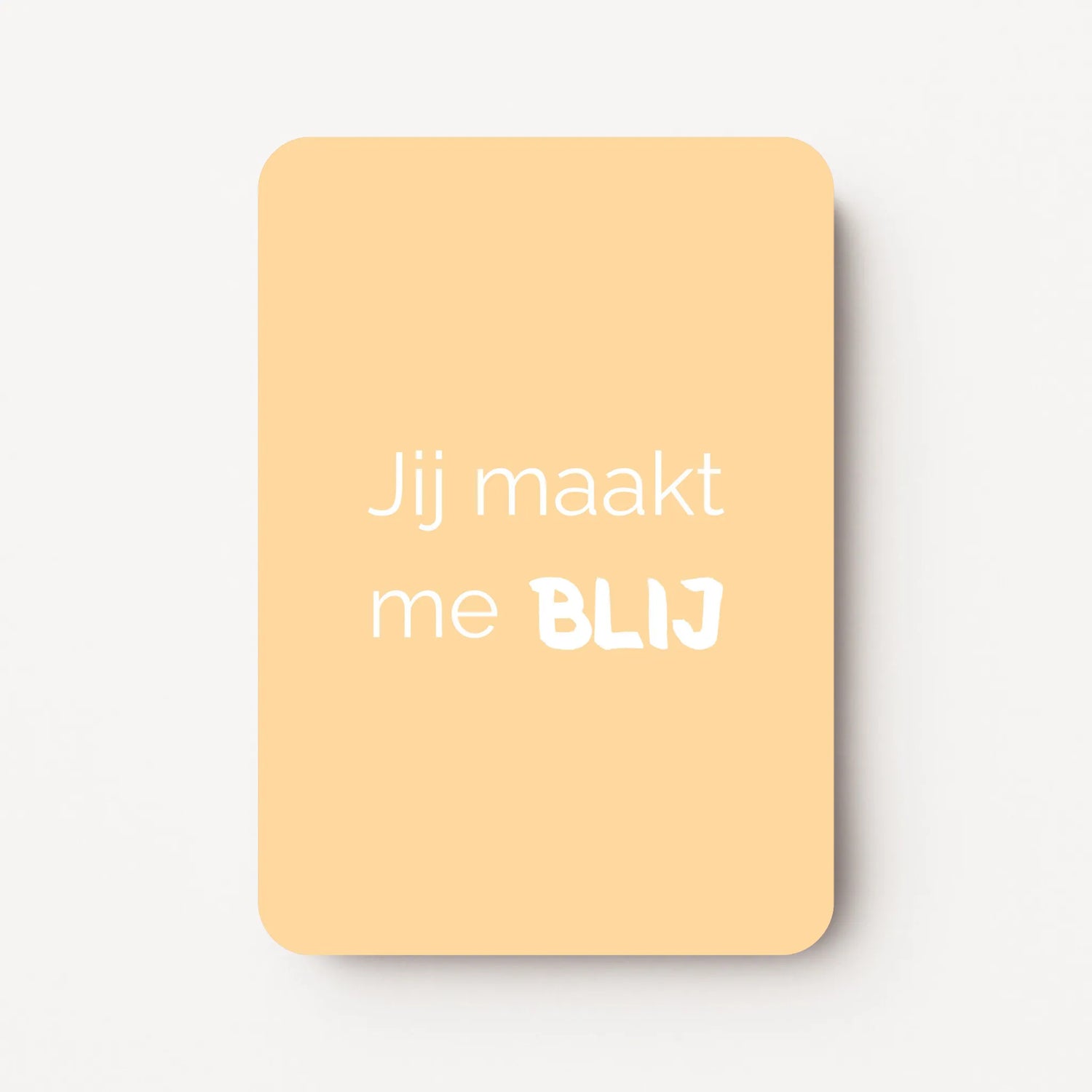 Staand minikaartje met witte tekst ‘Jij maakt me BLIJ’, minimalistisch ontwerp op een zachte abrikoos-gele achtergrond, flatlay op witte ondergrond.