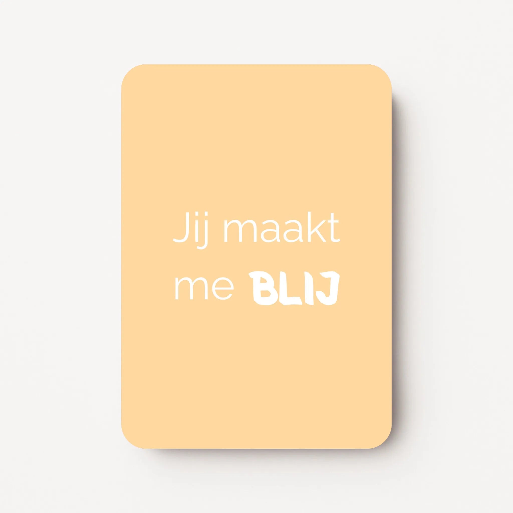 Staand minikaartje met witte tekst ‘Jij maakt me BLIJ’, minimalistisch ontwerp op een zachte abrikoos-gele achtergrond, flatlay op witte ondergrond.