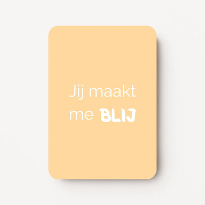 Staand minikaartje met witte tekst ‘Jij maakt me BLIJ’, minimalistisch ontwerp op een zachte abrikoos-gele achtergrond, flatlay op witte ondergrond.