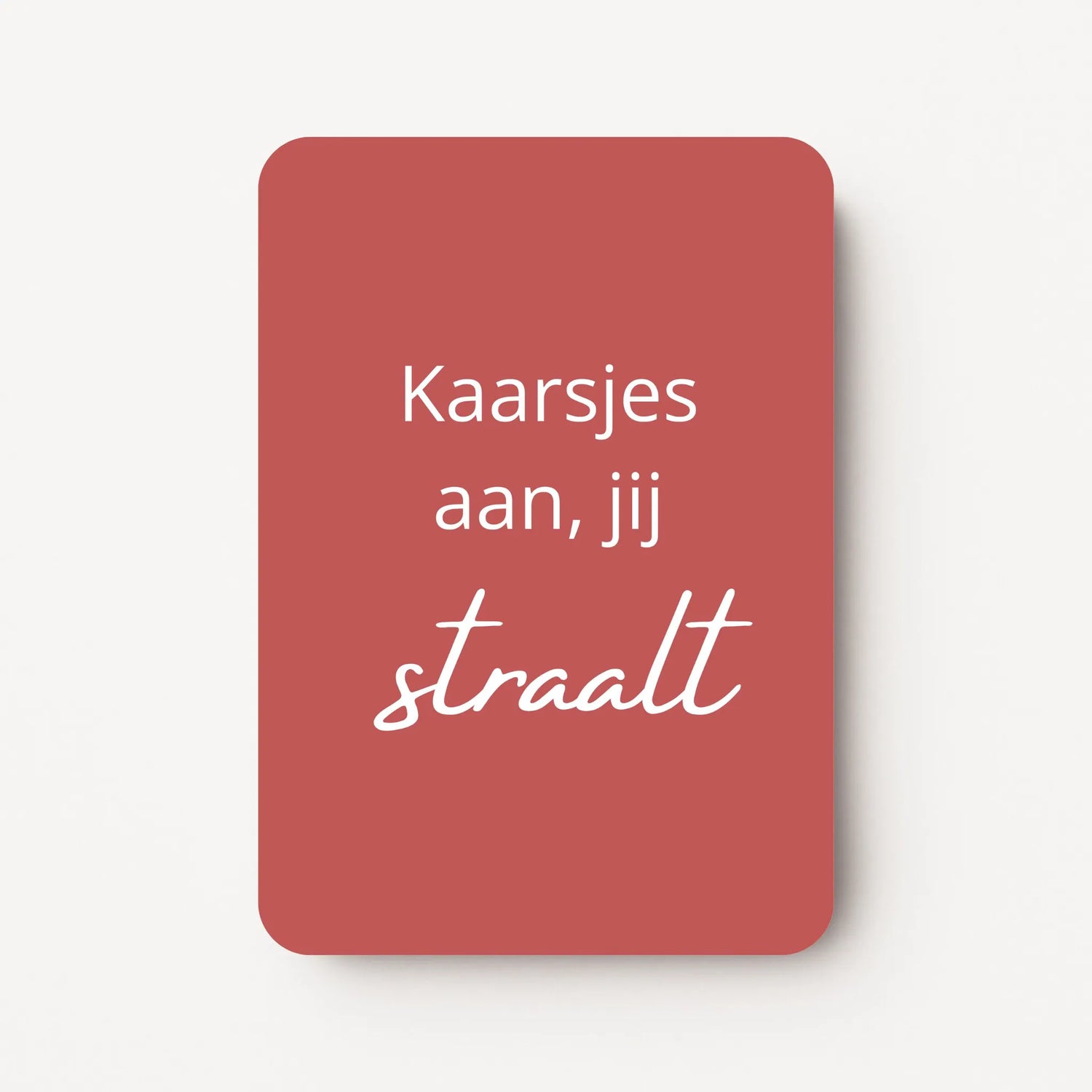 Staand minikaartje met witte tekst ‘Kaarsjes aan, jij straalt’, minimalistisch ontwerp op warme roodbruine achtergrond, flatlay op witte ondergrond.