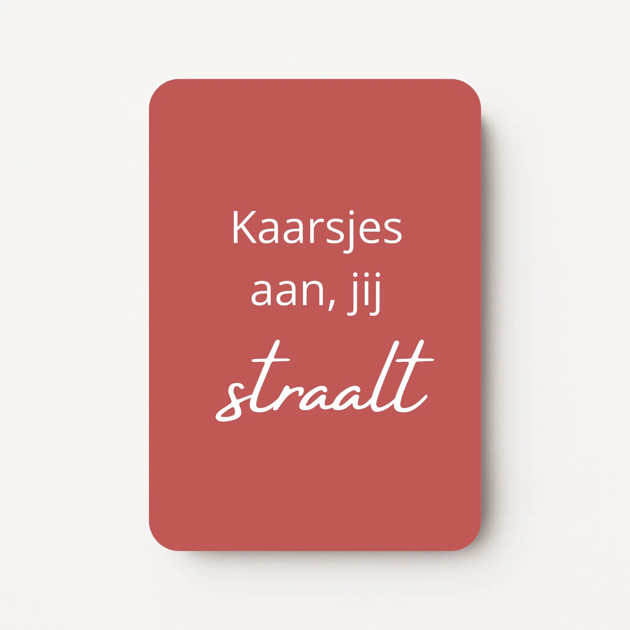 Staand minikaartje met witte tekst ‘Kaarsjes aan, jij straalt’, minimalistisch ontwerp op warme roodbruine achtergrond, flatlay op witte ondergrond.