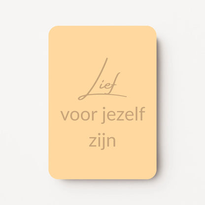 Staand minikaartje met tekst ‘Lief voor jezelf zijn’ in goudbeige letters, minimalistisch ontwerp op een zachte perzikgele achtergrond, flatlay op witte ondergrond.