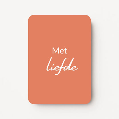 Staand minikaartje met witte tekst ‘Met liefde’, minimalistisch ontwerp op een warme koraalroze achtergrond, flatlay op witte ondergrond.