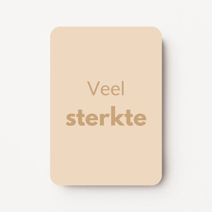 Staand minikaartje met goudbeige tekst ‘Veel sterkte’, minimalistisch ontwerp op een warme zandbeige achtergrond, flatlay op witte ondergrond.
