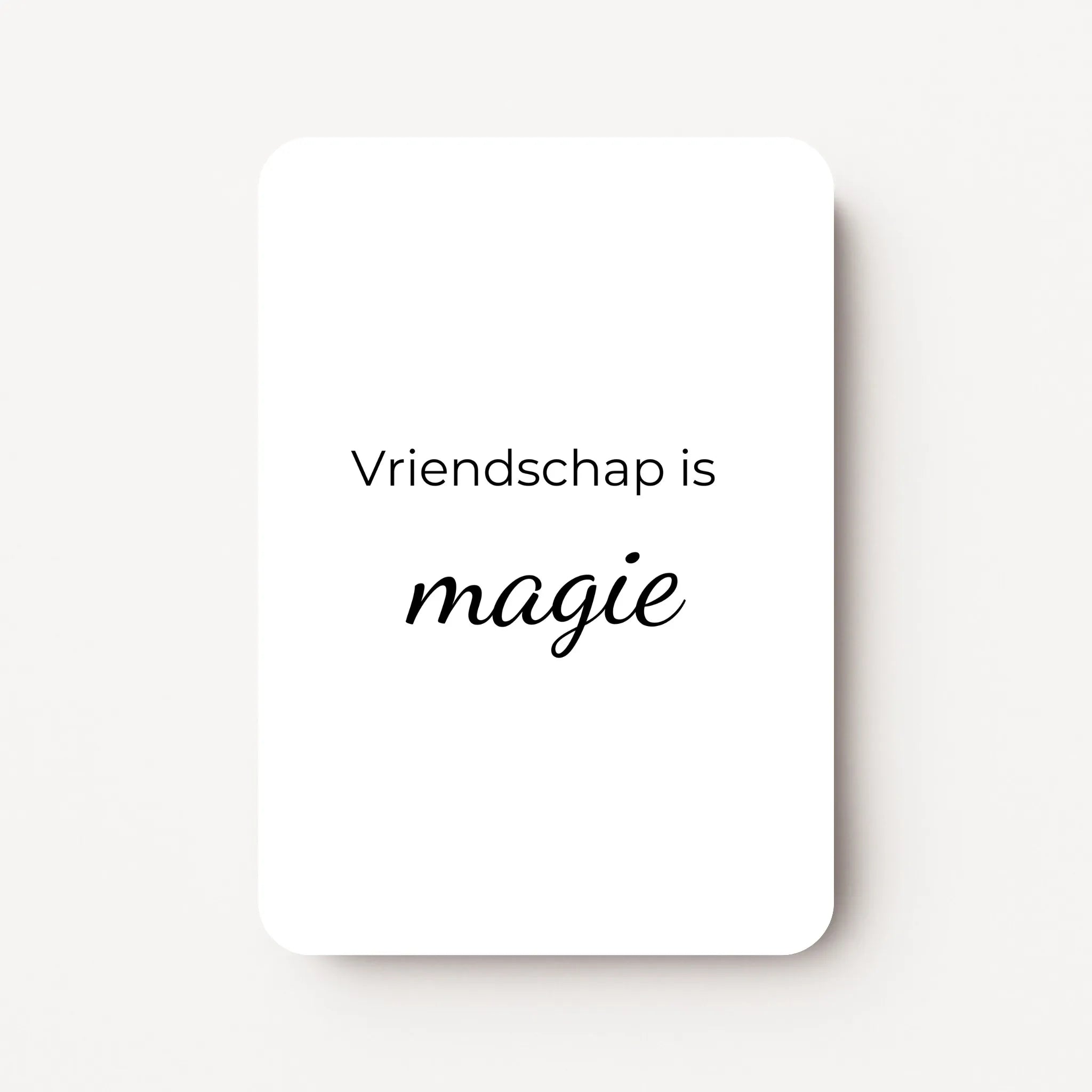Staand minikaartje met zwarte tekst ‘Vriendschap is magie’, minimalistisch ontwerp op witte achtergrond, flatlay op witte ondergrond.