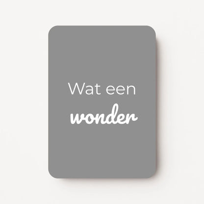 Staand minikaartje met tekst ‘Wat een wonder’ in witte letters, minimalistisch ontwerp op koel middengrijze achtergrond, flatlay op witte ondergrond.