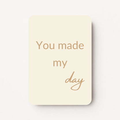 Staand minikaartje met tekst ‘You made my day’ in goudbeige letters, minimalistisch ontwerp op zachte crème achtergrond, flatlay op witte ondergrond.