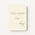 Staand minikaartje met tekst ‘You made my day’ in goudbeige letters, minimalistisch ontwerp op zachte crème achtergrond, flatlay op witte ondergrond.