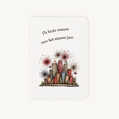 Staande dubbelgevouwen nieuwjaarskaart met afgeronde hoekjes en aquarelillustratie van kleurrijke flatgebouwen met sprankelend vuurwerk, omlijst door sierlijke tekst ‘De beste wensen voor het nieuwe jaar’, flatlay op lichte achtergrond.
