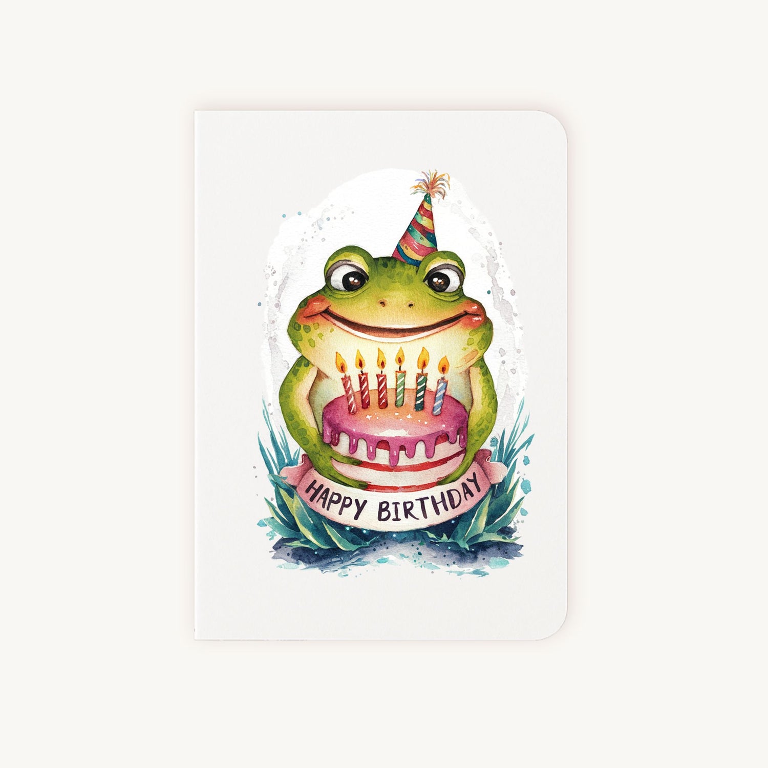 Handgemaakte verjaardagskaart met kikker, feesthoedje en taartje, rechtopstaand gefotografeerd.