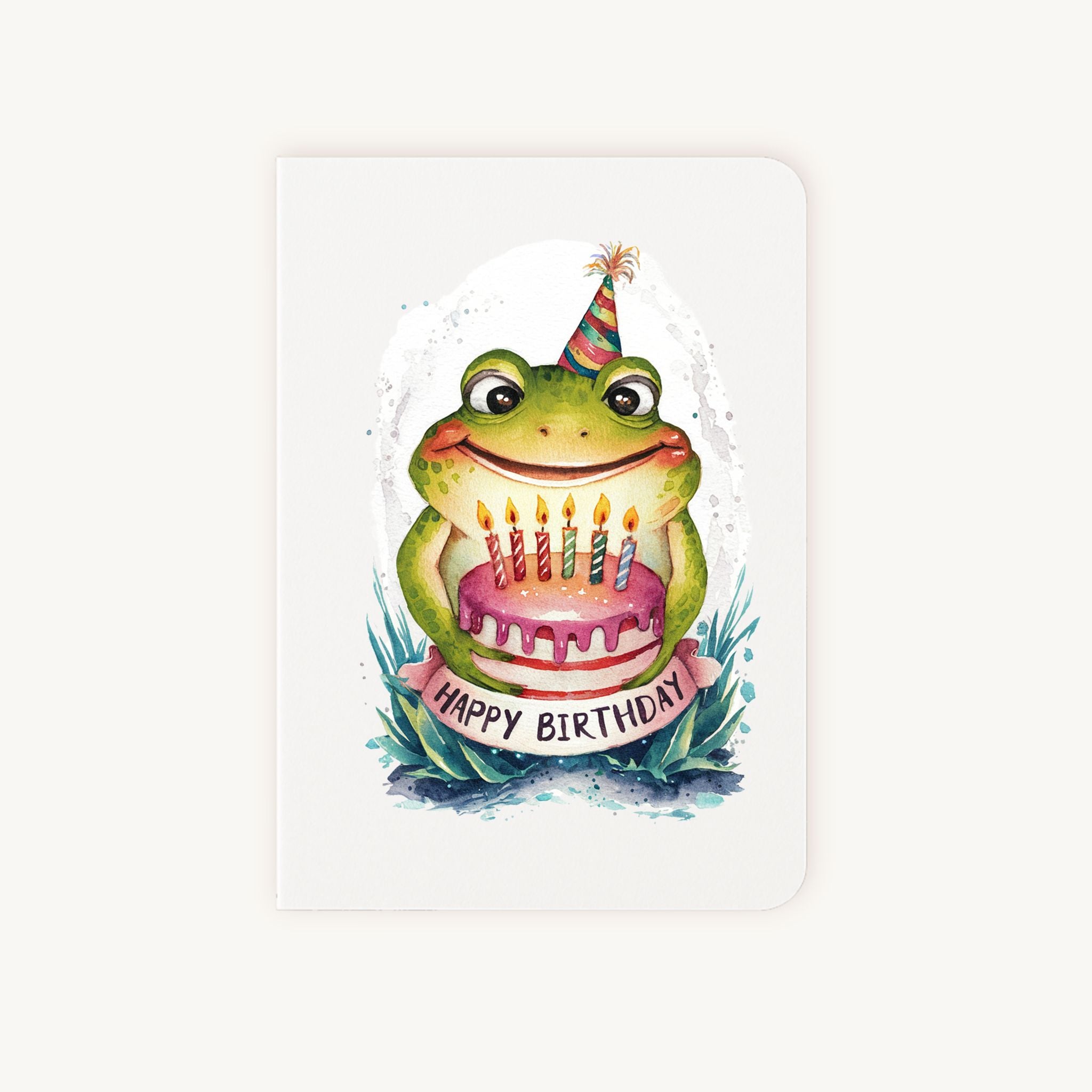 Handgemaakte verjaardagskaart met kikker, feesthoedje en taartje, rechtopstaand gefotografeerd.