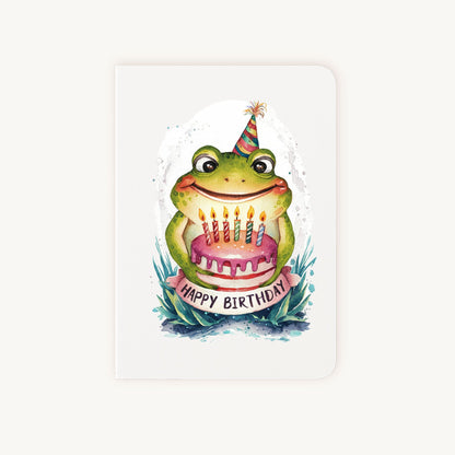 Handgemaakte verjaardagskaart met kikker, feesthoedje en taartje, rechtopstaand gefotografeerd.