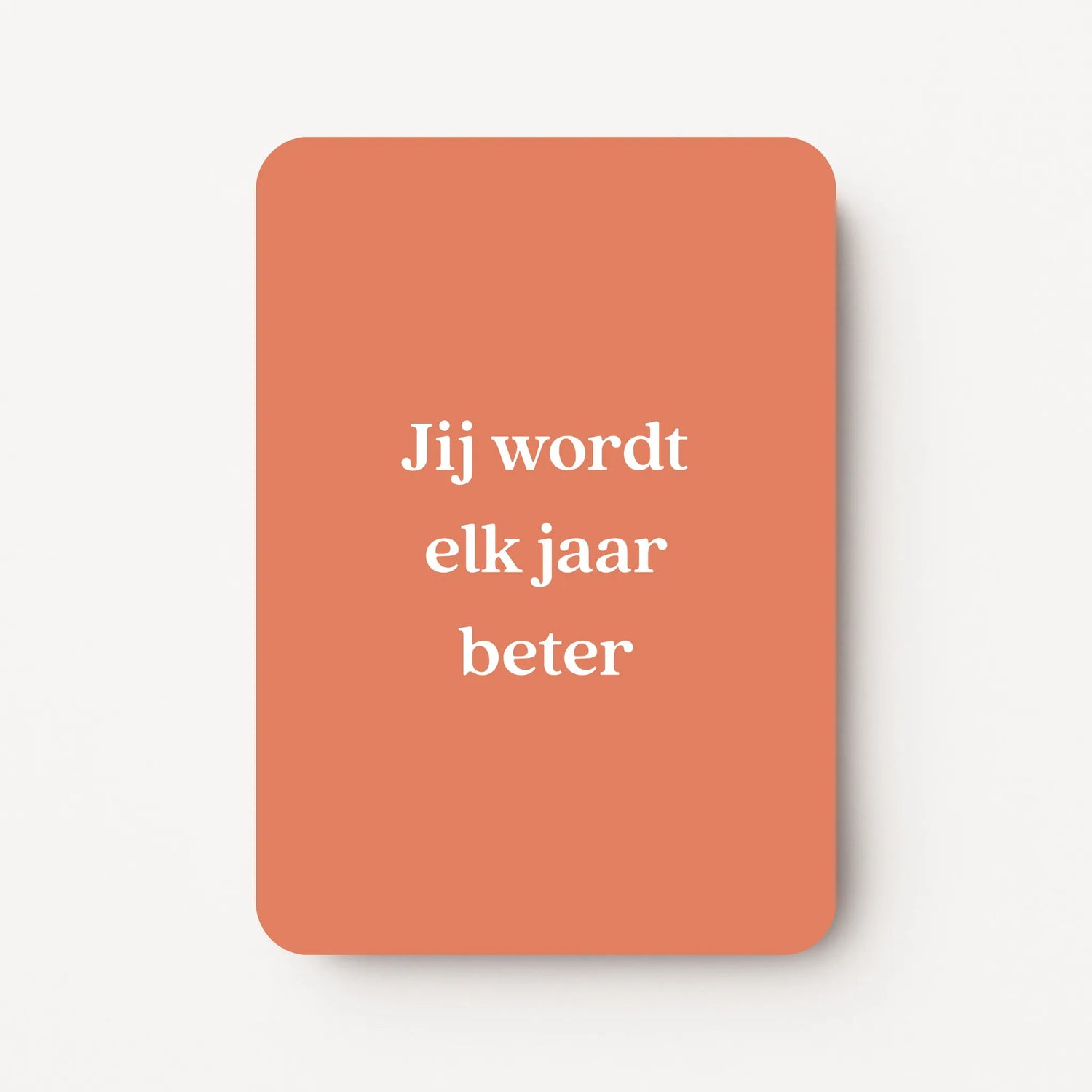 Staande verjaardagskaart voor een man met witte tekst ‘Jij wordt elk jaar beter’ op een warme oranje achtergrond, minimalistisch ontwerp, flatlay op witte ondergrond.