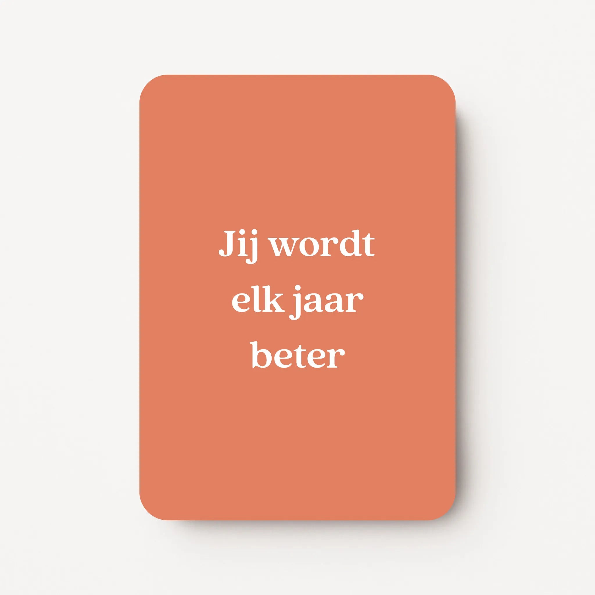 Staande verjaardagskaart voor een man met witte tekst ‘Jij wordt elk jaar beter’ op een warme oranje achtergrond, minimalistisch ontwerp, flatlay op witte ondergrond.