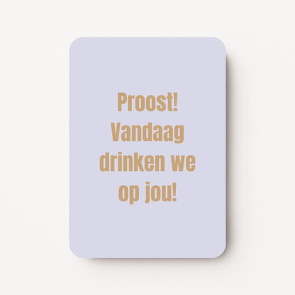 Staande verjaardagskaart voor mannen met goudbeige tekst ‘Proost! Vandaag drinken we op jou!’ op een lichtblauwe achtergrond, flatlay op witte ondergrond.