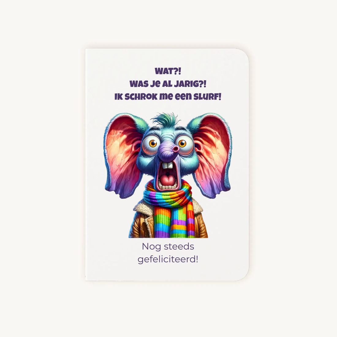 Staande dubbelgevouwen verjaardagskaart met cartoonachtige geschrokken olifant met grote oren en kleurrijke sjaal, met humoristische tekst Wat?! Was je al jarig? Ik schrok me een slurf! Nog steeds gefeliciteerd, flatlay op lichte achtergrond.