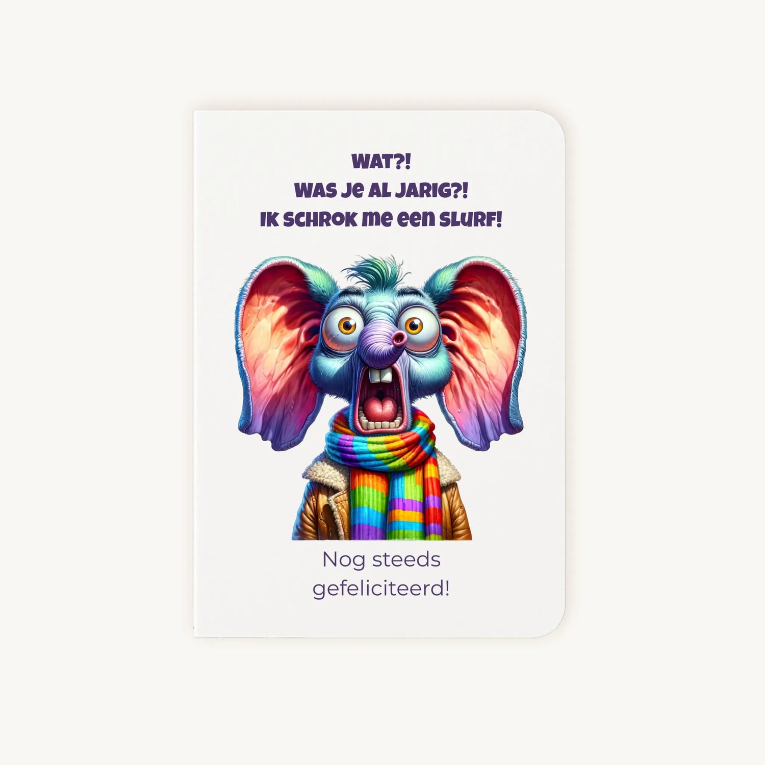 Staande dubbelgevouwen verjaardagskaart met cartoonachtige geschrokken olifant met grote oren en kleurrijke sjaal, met humoristische tekst Wat?! Was je al jarig? Ik schrok me een slurf! Nog steeds gefeliciteerd, flatlay op lichte achtergrond.