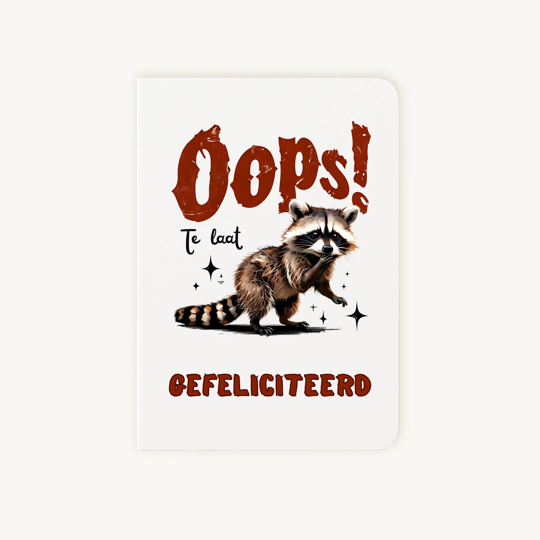 Staande dubbelgevouwen verjaardagskaart met schattige wasbeer en tekst ‘Oops! Te laat GEFELICITEERD’, flatlay op lichte achtergrond