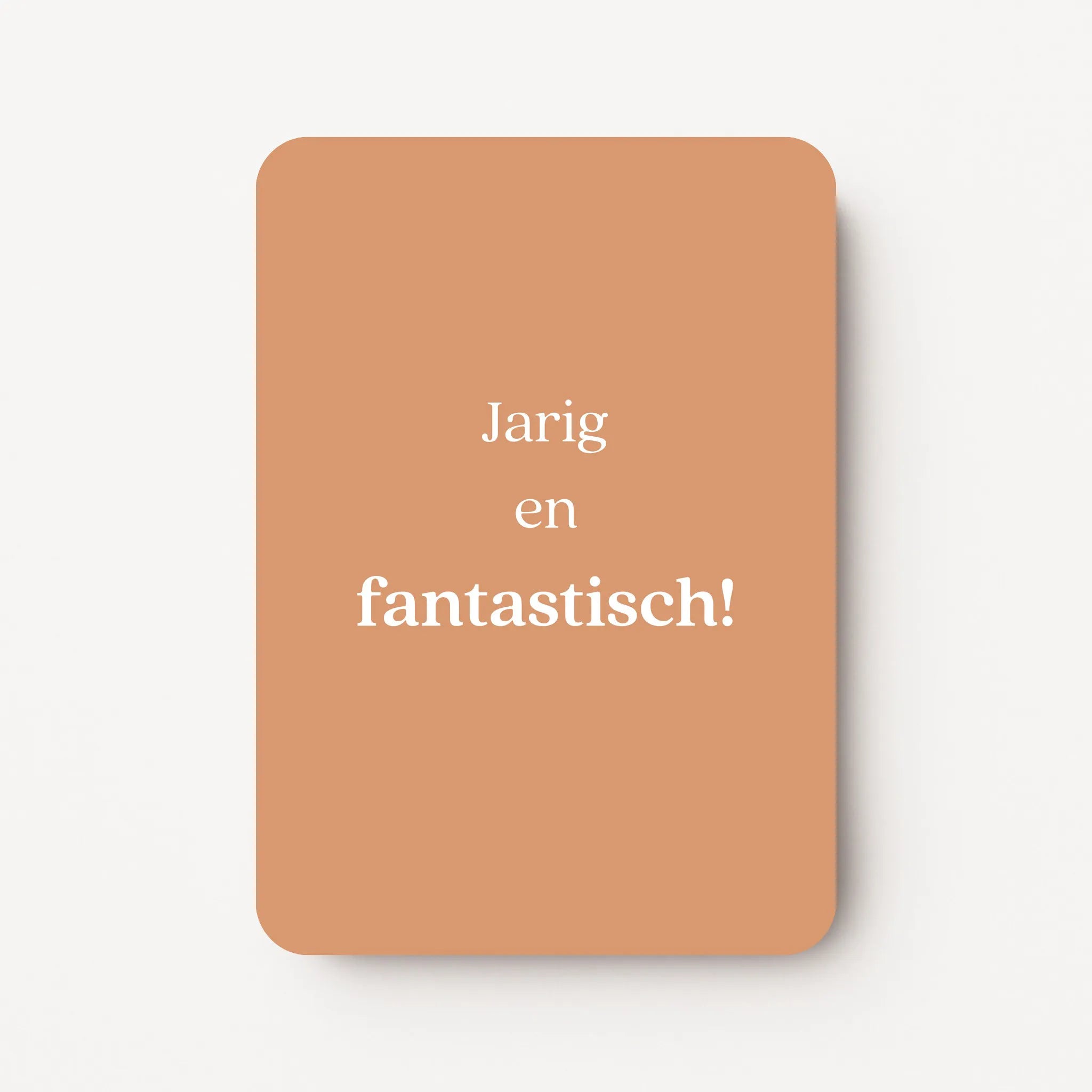 Staande verjaardagskaart voor een vrouw met witte tekst ‘Jarig en fantastisch!’ op een warme zandkleurige achtergrond, flatlay op witte ondergrond.