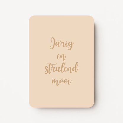 Staande zandkleurige verjaardagskaart met goudbruine tekst "Jarig en stralend mooi".
