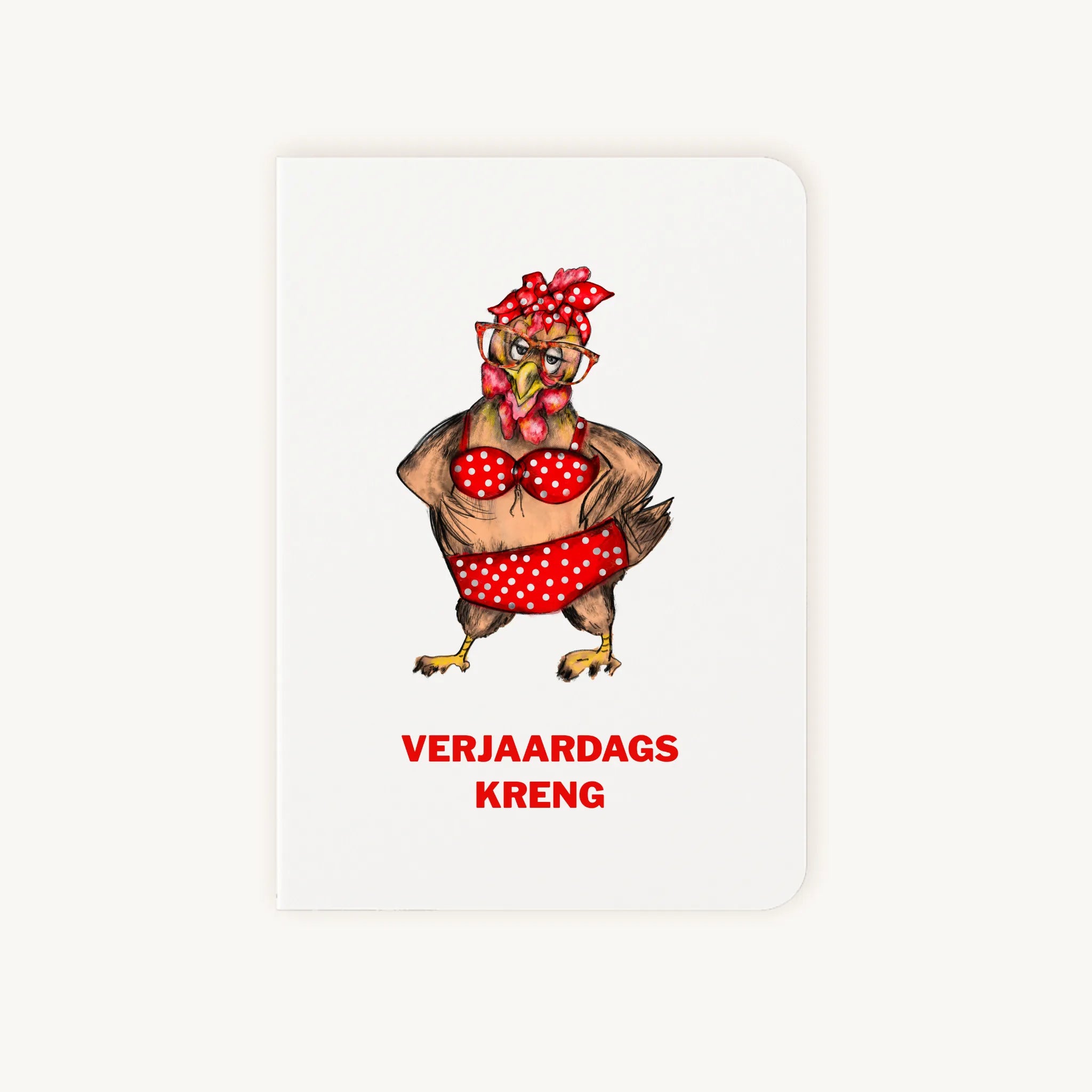 Staande dubbelgevouwen verjaardagskaart met grappige kip in knalrode bikini met stippen en strik, met tekst Verjaardags kreng, flatlay op lichte achtergrond.