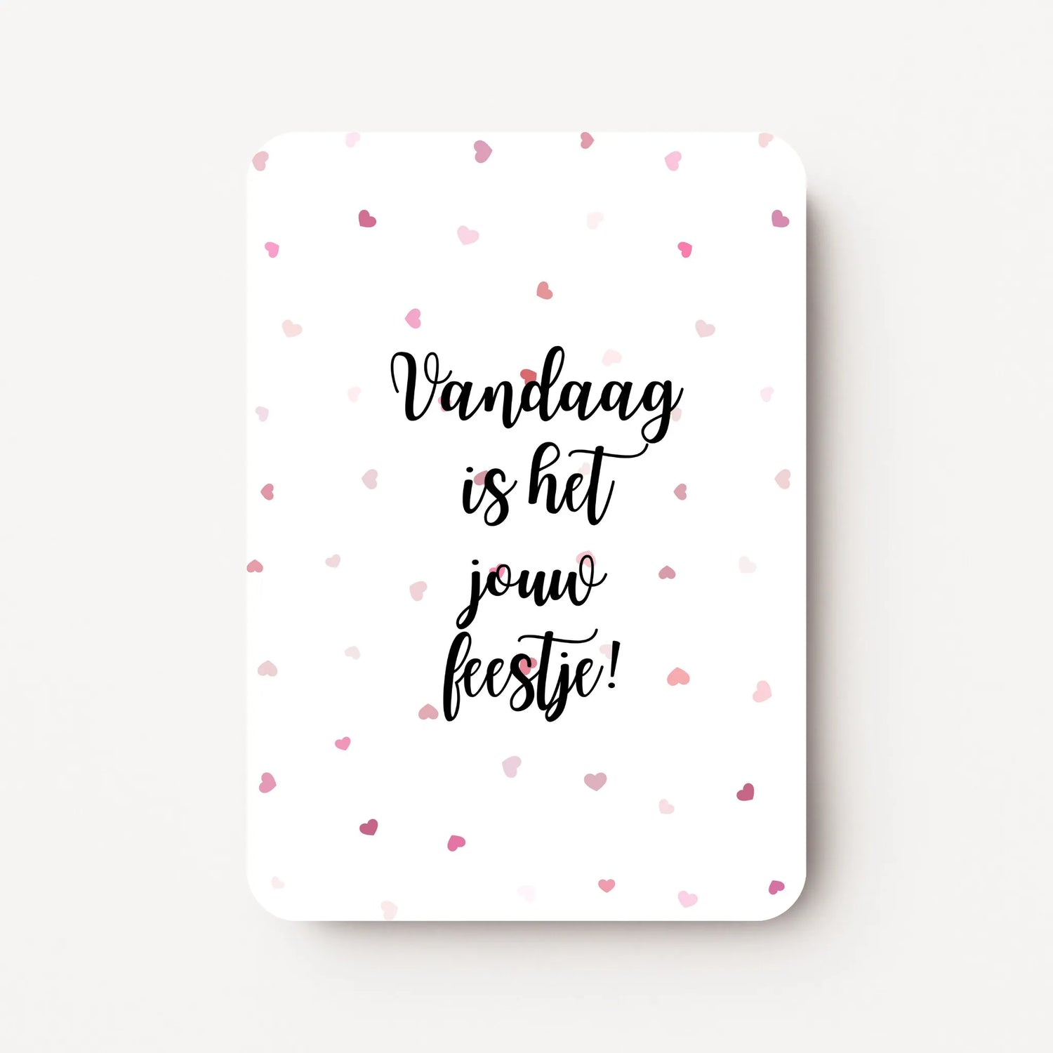 Staande verjaardagskaart voor een vrouw met zwarte tekst ‘Vandaag is het jouw feestje!’ en kleine roodroze hartjes verspreid over de witte achtergrond, flatlay op witte ondergrond.