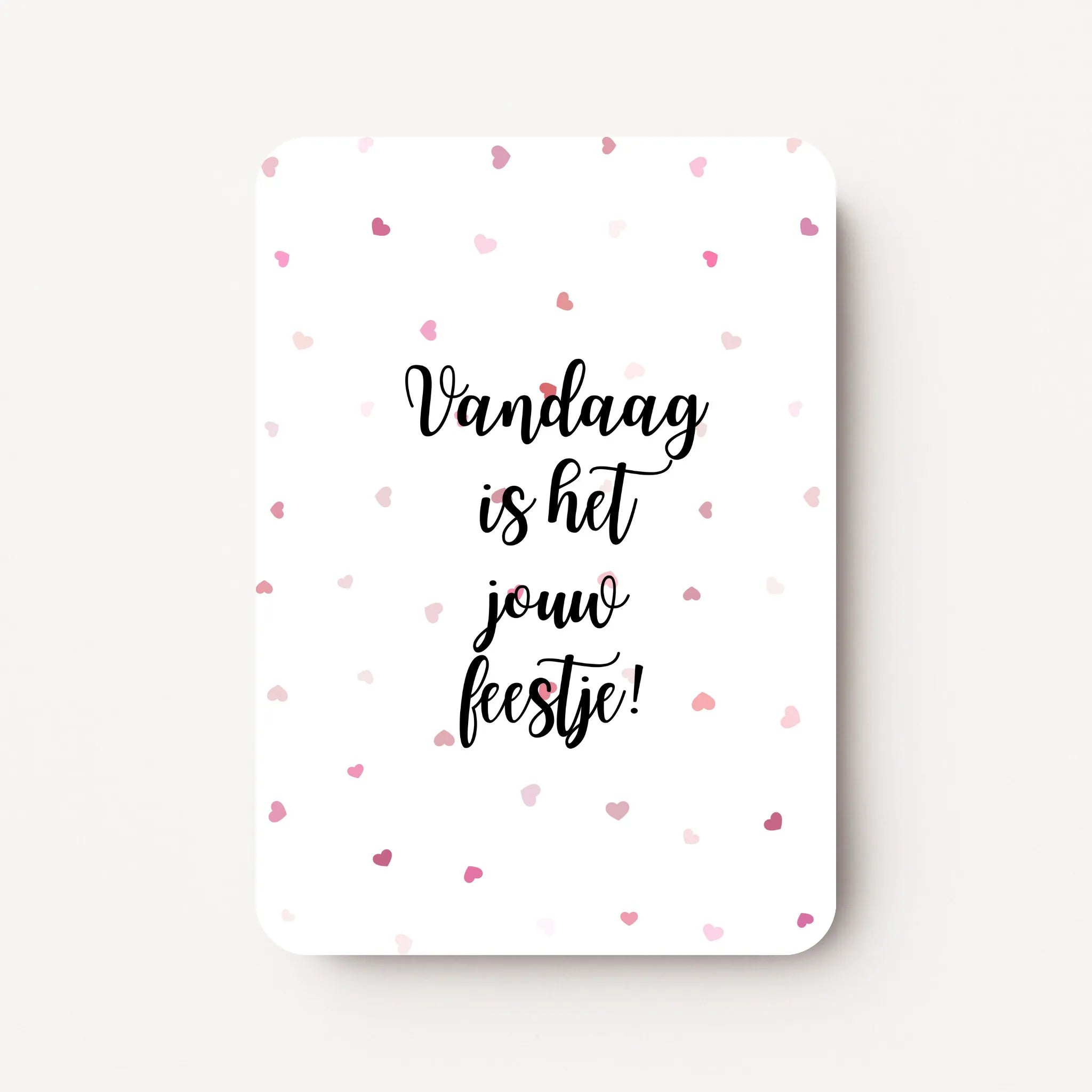 Staande verjaardagskaart voor een vrouw met zwarte tekst ‘Vandaag is het jouw feestje!’ en kleine roodroze hartjes verspreid over de witte achtergrond, flatlay op witte ondergrond.