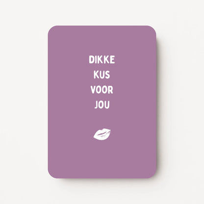 Staande kaart met tekst ‘Dikke kus voor jou’ in witte letters met witte lippenillustratie op een warme paarsroze achtergrond, flatlay op witte ondergrond.