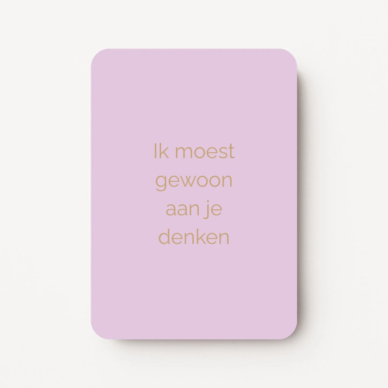 Staande kaart met tekst ‘Ik moest gewoon aan je denken’ in goudbruine letters op een zachte lila achtergrond, flatlay op witte ondergrond.