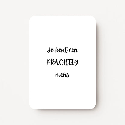 Staande kaart met zwarte tekst ‘Je bent een PRACHTIG mens’ op witte achtergrond, minimalistische stijl, flatlay op witte ondergrond.