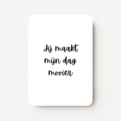 Staande zomaarkaart met zwarte tekst ‘Jij maakt mijn dag mooier’, minimalistisch ontwerp op witte achtergrond, flatlay op witte ondergrond.