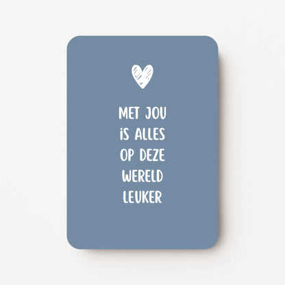 Staande kaart met tekst ‘Met jou is alles op deze wereld leuker’ in witte letters met een wit hartje, op een koele blauwgrijze achtergrond, flatlay op witte ondergrond.